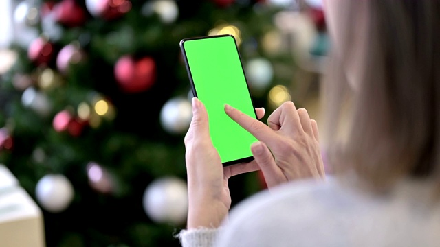 一名女性在圣诞装饰附近使用绿色模拟屏幕智能手机视频素材