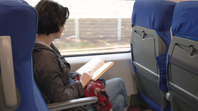 白人妇女坐在火车靠窗的位置看书火车在站台停视频下载