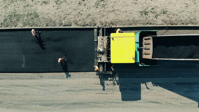 工人们正在从卡车上撒沥青。公路施工现场的沥青摊铺机。视频下载