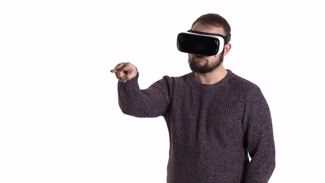 惊奇的年轻人使用虚拟现实眼镜。蓄着胡须的白人男子戴着虚拟现实眼镜，用两根手指指着自己的脸和摄像机视频素材