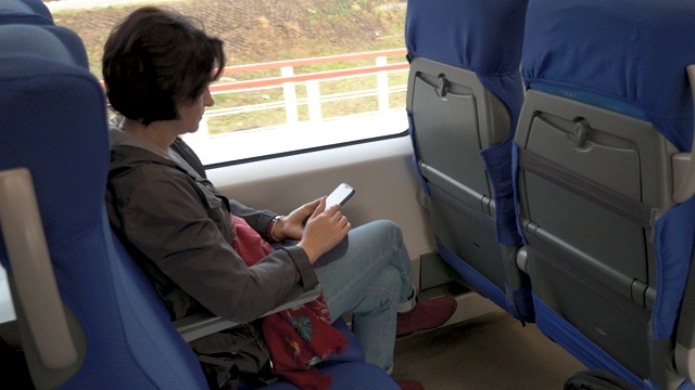 一名女子坐在火车上，手里拿着手机，点击后视图视频素材
