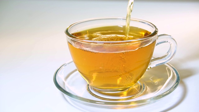 将香喷喷的红茶从茶壶中倒进白色背景上的透明玻璃茶杯中视频素材