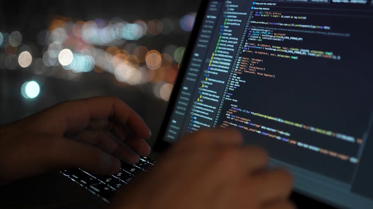 程序员编写开发网站的代码，以一个美丽的夜晚窗户为背景，城市灯光在散焦可见。视频下载