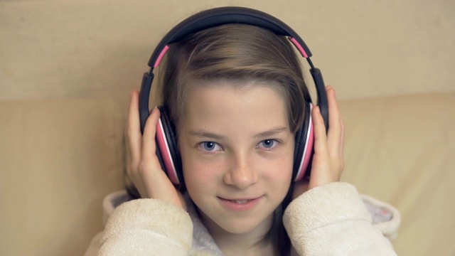 十几岁的女孩坐在沙发上戴着无线耳机听音乐视频下载