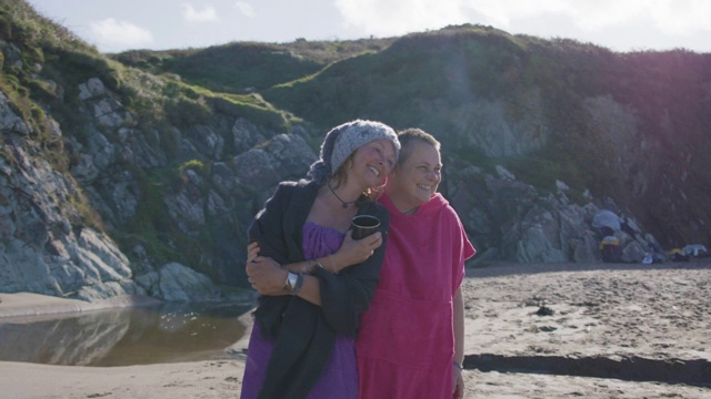 两个女人朋友在海里游泳后一起在空荡荡的海滩上大笑。视频素材