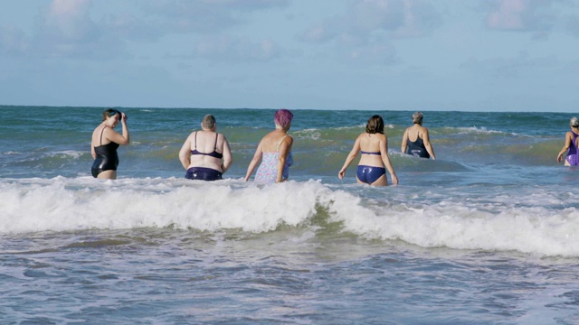 一群女游泳运动员在寒冷的海水中欢笑和跳跃。视频素材