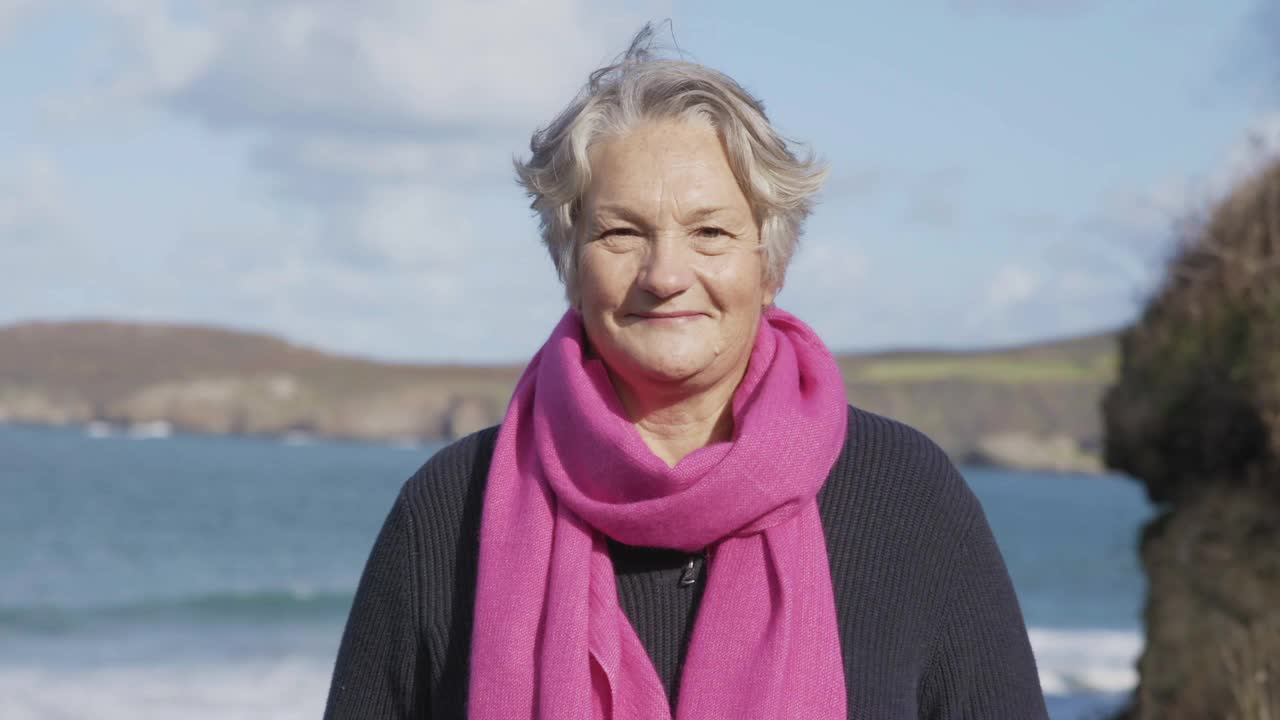一个女人微笑着对镜头的肖像，大海和海岸线在她身后。视频下载