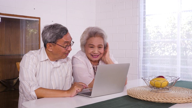 幸福的亚洲老年夫妇使用笔记本电脑在家里，家庭放松和花时间在一起在家里，退休人士和生活方式的概念视频素材