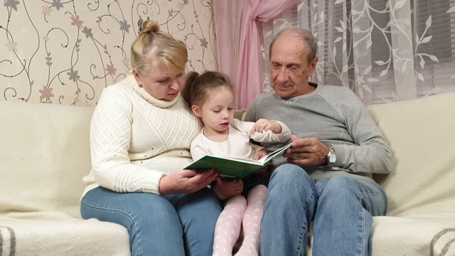 爷爷和奶奶正在看一本书，他们的孙女坐在家里的沙发上视频下载