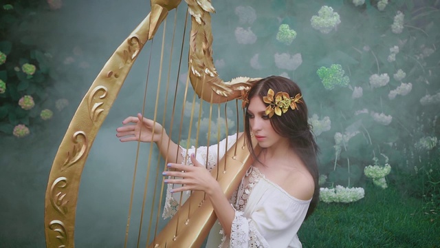 温柔的女孩可爱的天使的脸弹奏着精灵歌曲的竖琴旋律。希腊女神视频素材