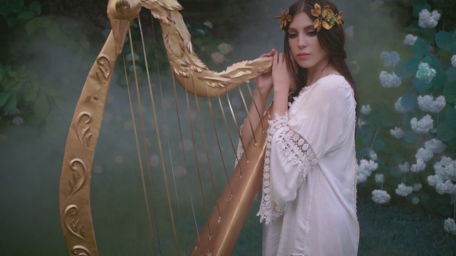 女孩的拥抱触摸精灵的老竖琴。戴金色月桂花环的希腊女神。视频素材
