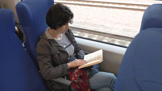 一个中等身材的女人坐在火车上。读一本书。视频素材