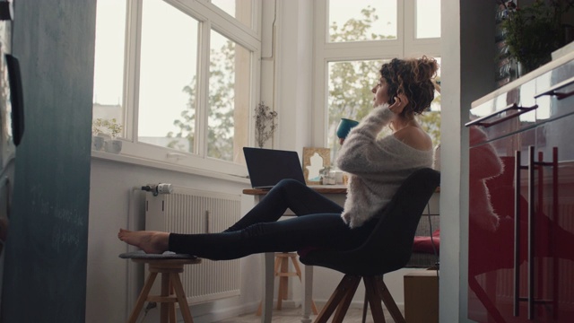 年轻女子坐在家里的笔记本电脑前喝咖啡视频素材