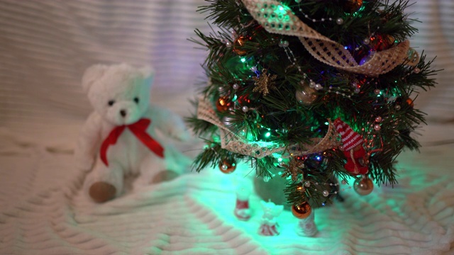 小圣诞泰迪熊坐在闪闪发光的圣诞树下。魔力四射的气氛，欢庆派对和圣诞的心情视频素材