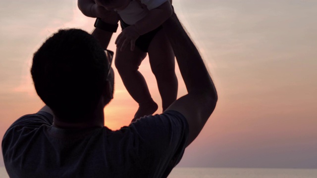 日落时分，快乐的父亲和愉快的男婴在海滩上的剪影。、家庭关系、童年及亲子观念。东南亚和东亚:亚洲婴儿视频素材