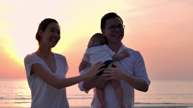 剪影快乐的父亲，母亲，婴儿儿子与乐趣沿着海边的日落海浪在沙滩上。积极的父母和人在暑假与孩子户外活动。幸福的家庭假期。视频素材