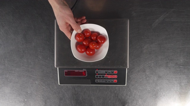 一只手将一个盛有樱桃番茄的碗放到电子秤上称量。为烹饪膳食食物准备配料。健康食品的概念视频下载