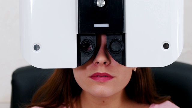 眼科治疗——一个有着亮粉色嘴唇的年轻女子用一种特殊的验光设备检查她的视力——她闭着眼睛在机器上说话视频下载