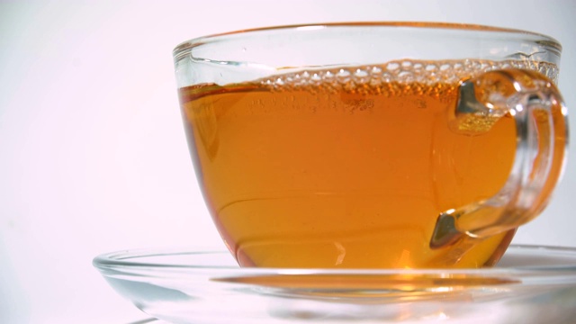 将香喷喷的红茶从茶壶中倒进白色背景上的透明玻璃茶杯中视频素材