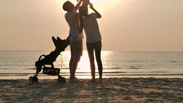 剪影快乐的父亲，母亲，婴儿儿子有乐趣沿海边的日落海浪在沙滩上。积极的父母和人在暑假带宝宝户外活动。幸福的家庭假期。家庭，生活方式，人，生命保险，假期-股票视频素材