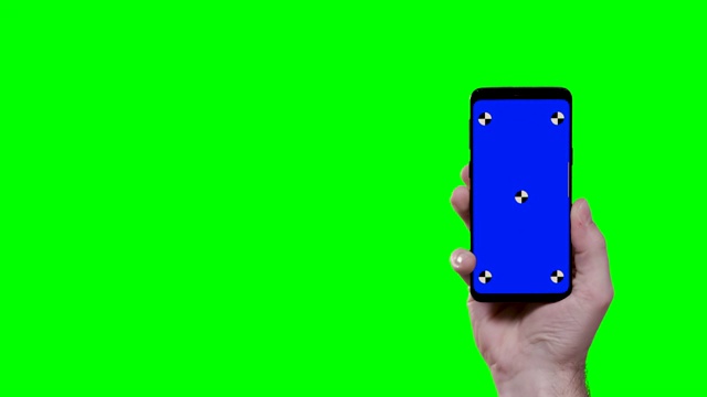 男子手持智能手机与蓝色croma键跟踪点和绿色屏幕在背景进入屏幕的右侧视频素材