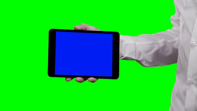 一名身穿白色衬衫的男子手持平板电脑水平进入相机，蓝色的croma键和绿色的屏幕为背景视频素材