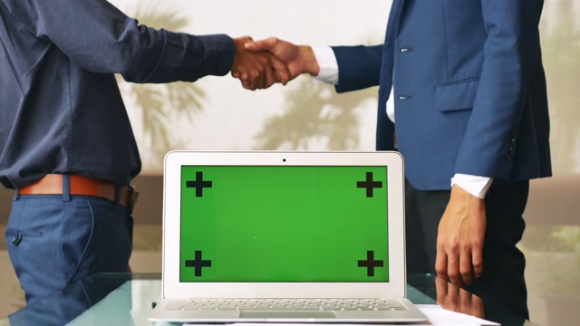 两个商人在办公室靠窗边握手交谈，手提电脑是绿屏的视频素材
