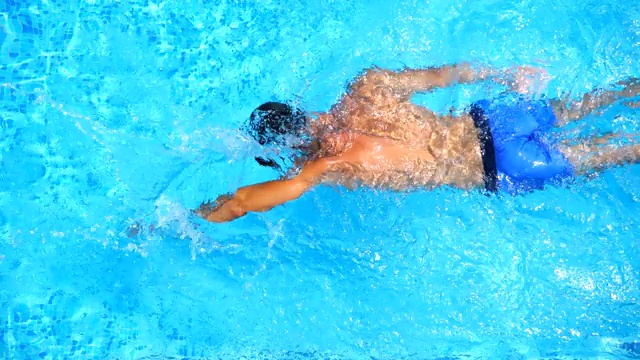 一个肌肉发达的男人在游泳池里游泳，溅起水花。在阳光明媚的日子里，年轻的运动男孩漂浮在豪华酒店的盆地上。在热带度假胜地放松的运动员。暑假的概念。俯视图视频下载
