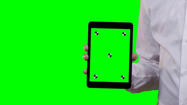 一名身穿白衬衫的男子手持平板电脑对着摄像头，智能手机的前景和背景跟踪点都是绿色屏幕视频素材