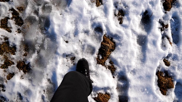 视角男性脚穿靴子踏过雪地。早春时节，年轻的徒步旅行者的双腿在雪地上行走。寒假或假期的概念。特写慢镜头视频素材