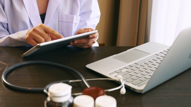 女医生在医院穿着医生制服与听诊器使用数字平板电脑和笔记本电脑视频素材