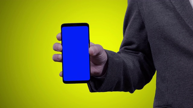一名穿着西装的男子拿着智能手机对着相机，黄色背景上的蓝色铬色键视频素材