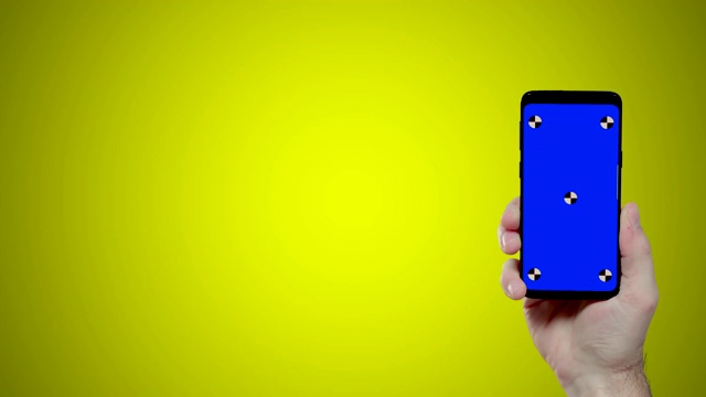 黄色背景上带有蓝色croma键跟踪点的男士手持智能手机进入屏幕右侧视频素材