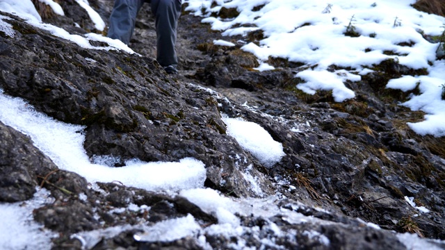 年轻的徒步旅行者的脚在旅行中走下岩石斜坡。男游客的双腿从雪山上滑下来。健康积极的生活方式。寒假或假期的概念。低视角慢动作视频素材