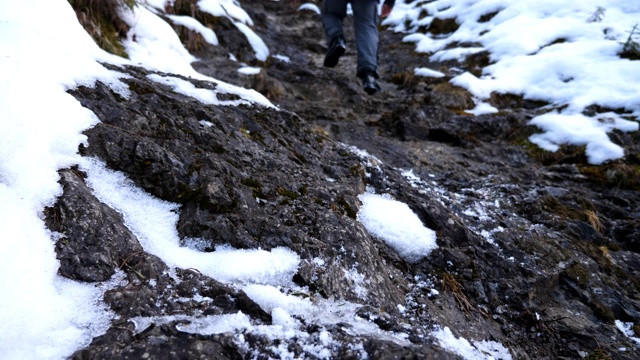 难以辨认的徒步者在旅途中爬上小山。年轻男性游客的双腿在岩石斜坡上徒步行走。健康积极的生活方式。寒假或假期的概念。后视图慢动作视频素材