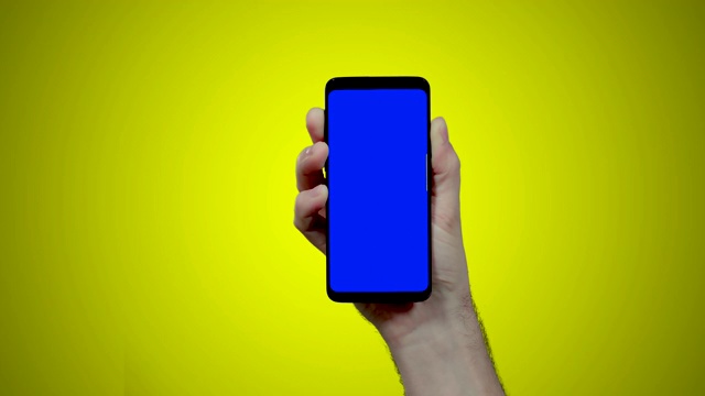 男子手持智能手机与蓝色croma键在黄色背景上双swipe到左边两次视频素材