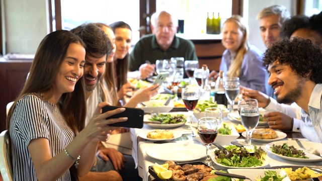 一名女子在餐厅与家人共进午餐时在手机上展示照片视频下载