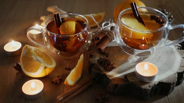 橙味茶与肉桂和小豆蔻杯，橙和肉桂棒点燃蜡烛在木桌上。木质背景上加了热葡萄酒和香料。有选择性的重点。关闭了。视频素材