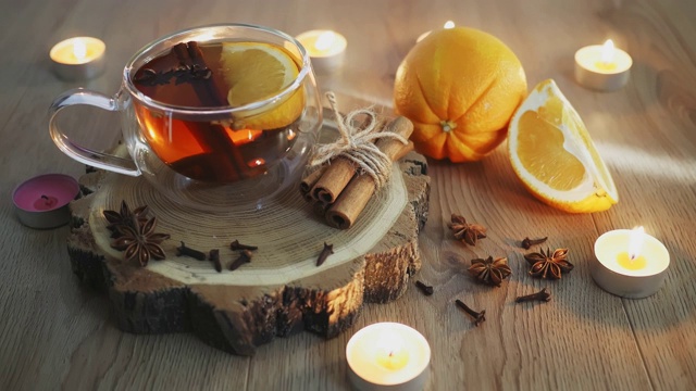 在杯中加入肉桂和小豆蔻的橙味茶周围放上蜡烛，在木桌上放上橘色和肉桂棒。木质背景上加了热葡萄酒和香料。有选择性的重点。近距离视频素材
