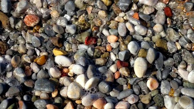 特写镜头。带着白色泡沫的柔软的海浪被冲到卵石滩上。美丽的，五颜六色的圆形海卵石在地中海沿岸，海岸。夏天炎热的一天。希腊视频素材