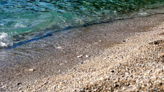 特写镜头。带着白色泡沫的柔软的海浪被冲到卵石滩上。美丽的，五颜六色的圆形海卵石在地中海沿岸，海岸。夏天炎热的一天。希腊视频素材