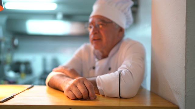 一个疲惫/忧虑的高级厨师在厨房柜台上视频下载