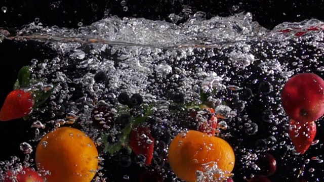 超级慢动作:在黑色背景下混合水果滴入淡水中视频素材