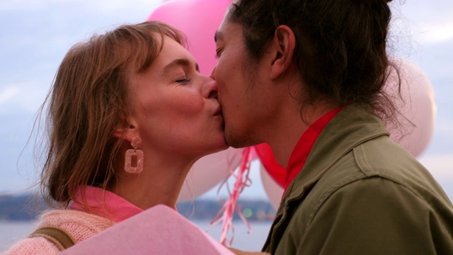 在情人节这天，一对情侣手捧气球和鲜花亲吻视频素材