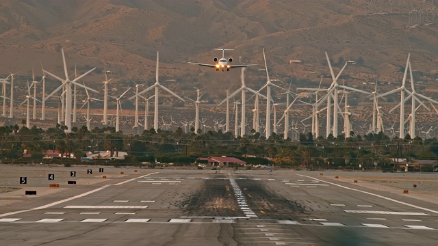LS客机客机降落在机场跑道上，背景是可再生能源风力发电场和高速公路上的汽车视频素材