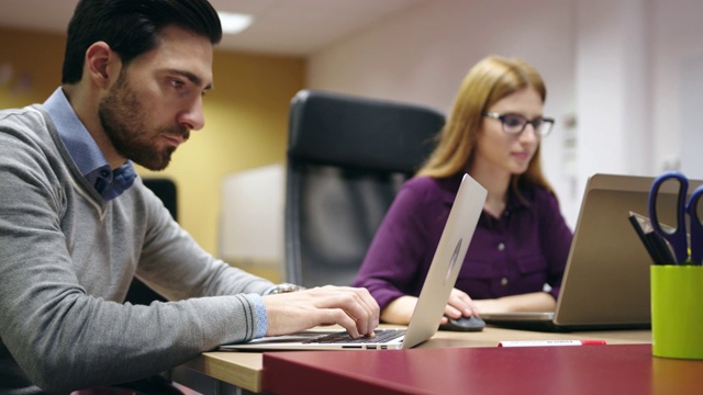 一名男子在和同事一起工作时用手指着笔记本电脑屏幕视频素材