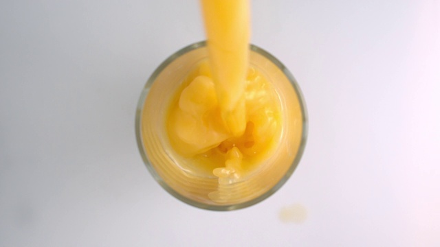 在白色的背景表面上用慢动作将橙汁倒入玻璃杯中视频素材
