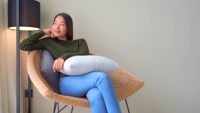 年轻的亚洲女人开心的微笑坐在沙发上视频下载