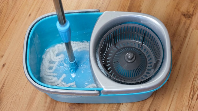 在装满水和洗涤剂的蓝色桶中清洗和旋转拖把伸缩手柄。视频下载