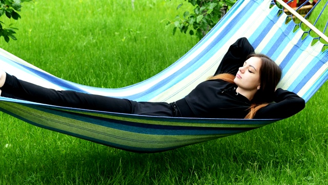 美丽的年轻女子躺在花园里的吊床上，休息和打瞌睡视频下载